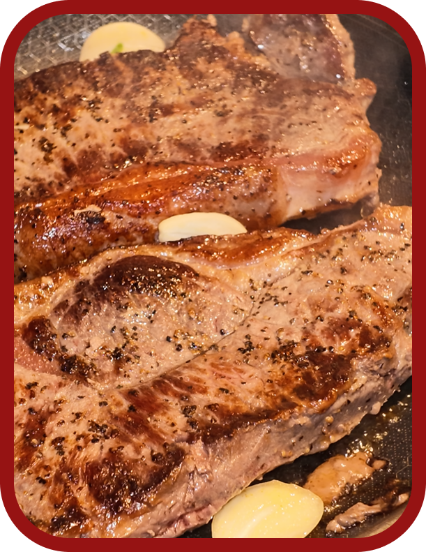 cooking-new-york-strip-steak Pan-searing Nutrafarms New York strip steaks with butter and garlic in a hot skillet.